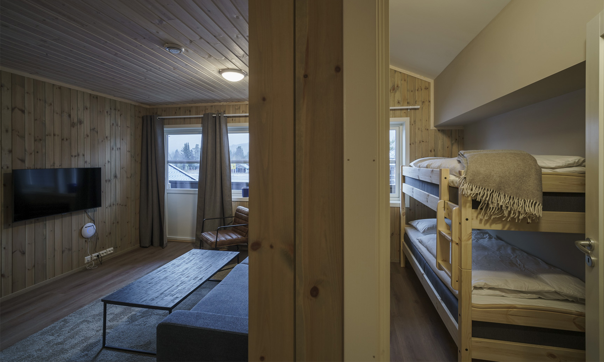 Oppholdsrom med sofa, TV og store vinduer mot fjellandskap.